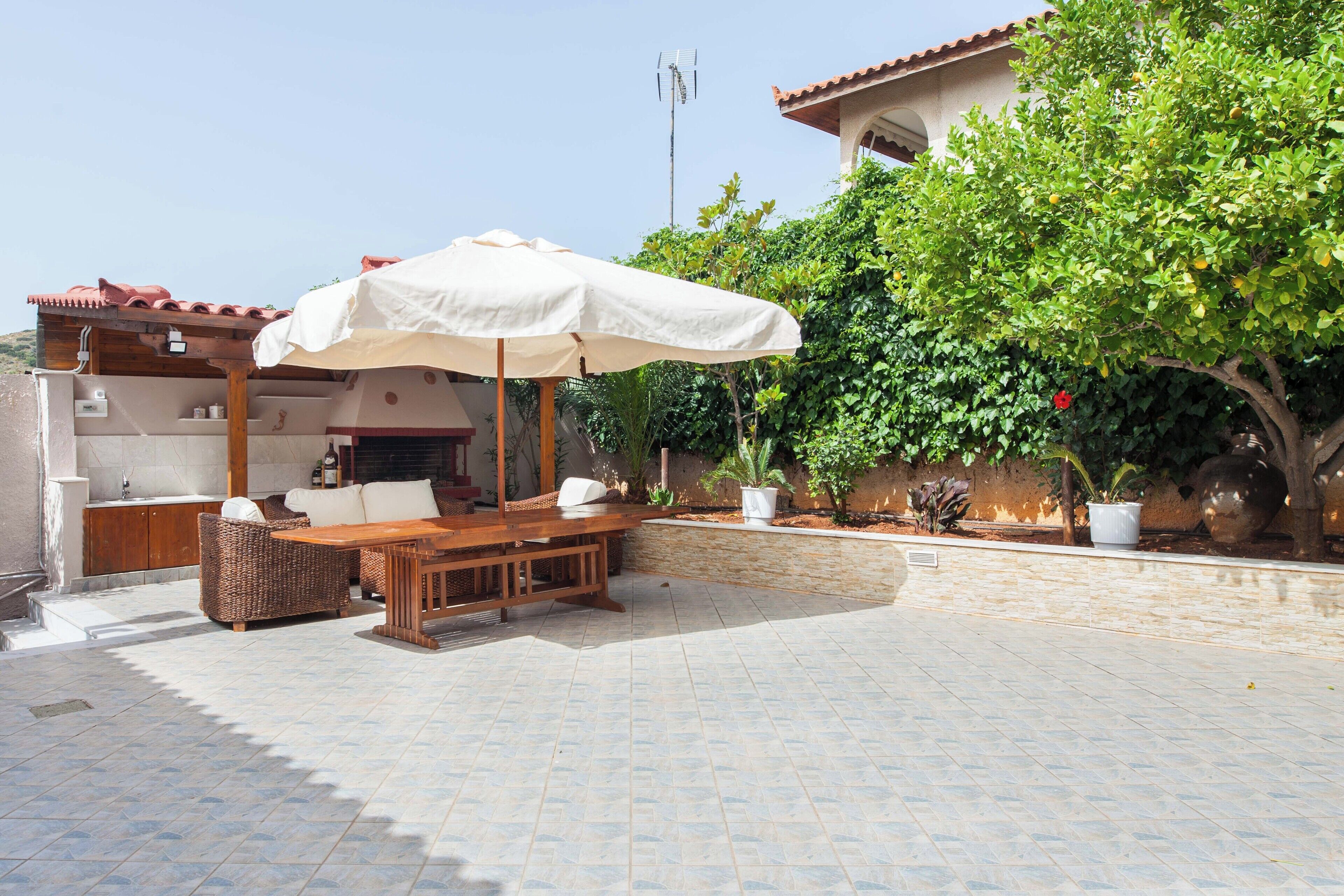 An outdoor patio with a wooden table and chairs, a white umbrella, and a stone wall.