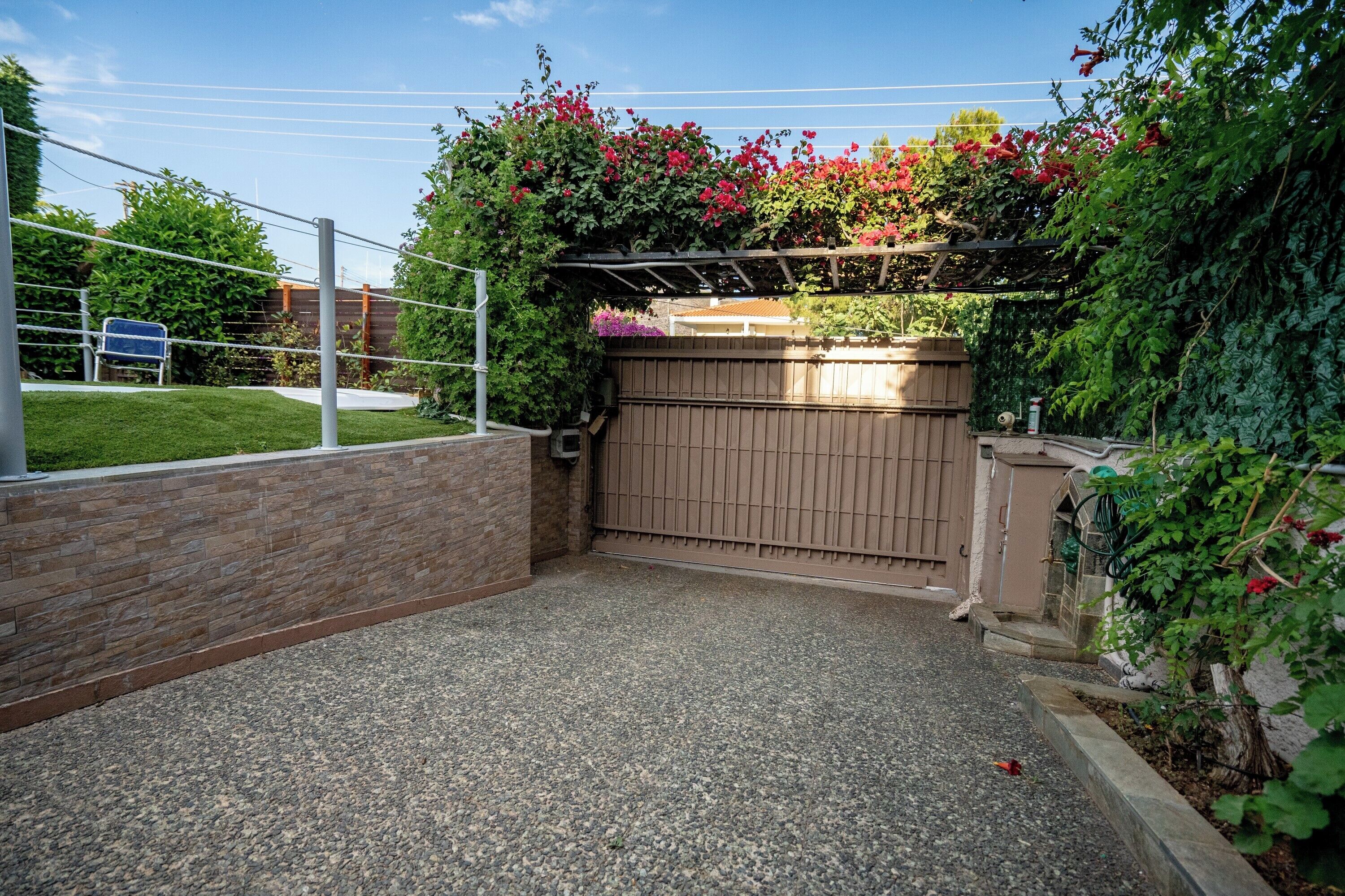 A gated driveway leading to a house with a brick wall on one side and a wooden fence on the other.