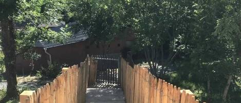 A wooden pathway leading to a traditional building with a tiled roof, surrounded by trees.