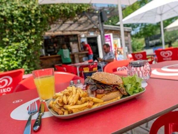 Ein Essen mit einem Burger, Pommes und einem Getränk auf einem roten Tisch.
