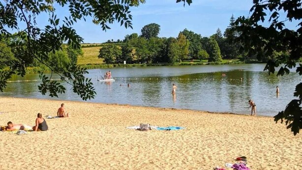Ein sandiger Strand mit Menschen, die sonnenbaden und im See schwimmen.