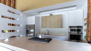 A modern kitchen with white cabinets, a central island with a stove, a refrigerator, and an oven. - Yeguas V60 by Wynwood House (Anapoima)