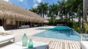 A pool area with a thatched-roof structure, lounge chairs, and a wooden deck. - Yeguas V60 by Wynwood House (Anapoima)