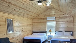 A cozy cabin-style room with a wooden ceiling, two beds, a sofa, a coffee table, and a desk with a chair. - Cabin 3 with AC and WiFi in charming Reed Point. ADA compliant. (Reed Point)