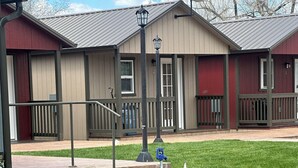 A building with a red exterior and beige siding, featuring a covered outdoor area with a metal railing and a bench. - Cabin 3 with AC and WiFi in charming Reed Point. ADA compliant. (Reed Point)