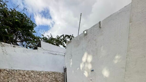 A rectangular outdoor bathtub with a stone wall and a white wall in the background.