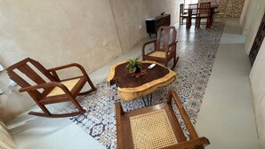 A dining area with a round wooden table, two wooden chairs, and a small side table with a plant.