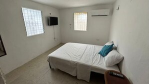 A small, clean room with a single bed, a TV mounted on the wall, and two windows providing natural light.