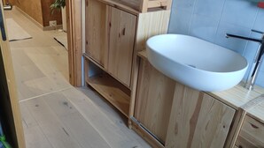 Un baño con tocador de madera, lavamanos blanco y grifo cromado.