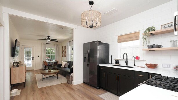 Una cocina moderna con un refrigerador negro, encimeras blancas y un comedor con mesa y sillas.
