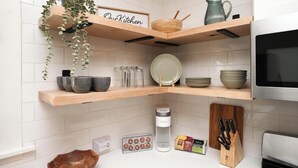 Una cocina con estantes de madera, un hervidor, una cafetera y un bloque de cuchillos.