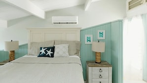 A bedroom with a bed, bedside tables, an air conditioning unit, and wall-mounted artwork.