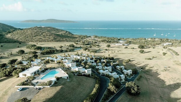 An aerial view of a resort with multiple white buildings, a swimming pool, and a view of the ocean.