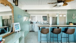 A modern kitchen with a central island, bar stools, stainless steel appliances, and a decorative ceiling fan.