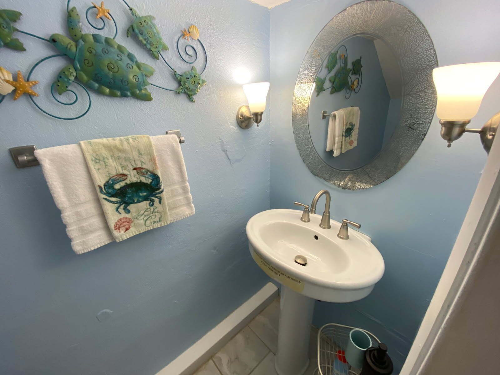 Une salle de bain avec un lavabo, un porte-serviettes sur lequel est posée une serviette, un mur décoratif représentant des créatures marines, et un miroir sur lequel est accrochée une serviette.