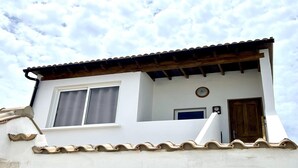 Un edificio blanco con techo de tejas, una puerta de madera y una ventana con cortinas.