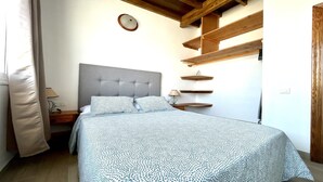 Un dormitorio con cama, mesita de noche, lámpara, un reloj de pared y estantes de madera.