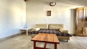 Una habitación con una mesa de madera, dos sofás beige con cojines estampados, una mesita auxiliar blanca, un cuadro en la pared y una puerta de madera.