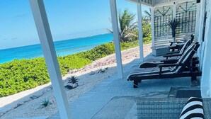 A covered outdoor seating area with a view of the ocean, featuring striped cushions and a bowl of snacks.