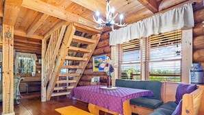 A wooden cabin interior with a dining table, bench, sofa, and a ladder to a loft.