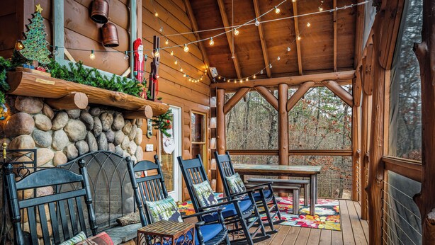 A cozy wooden cabin with a stone fireplace, rocking chairs, and a string of lights.