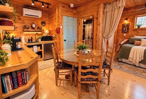 L’intérieur d’un chalet en bois chaleureux et accueillant, avec une table à manger, des chaises, une bibliothèque, un coin cuisine et un lit.