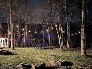 Ein Campingplatz mit Picknicktisch und Lichterkette in einer bewaldeten Gegend bei Nacht.