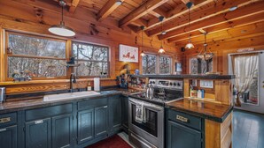 A cabin-style kitchen with wooden beams, a large window, and a red rug.