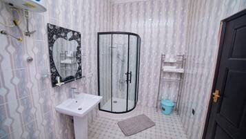 Une salle de bain dotée d’une douche à parois courbes en verre, d’un lavabo blanc, d’un miroir orné de motifs floraux et d’un papier peint à motifs.