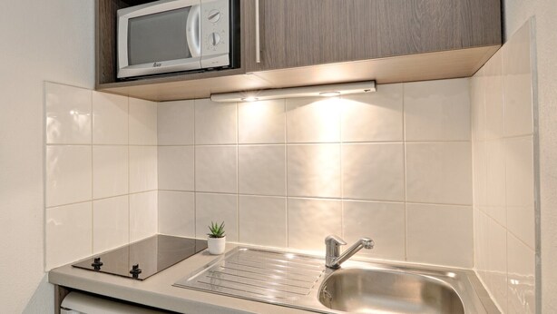 Een kleine keuken met een magnetron, een spoelbak en een vaatwasser.