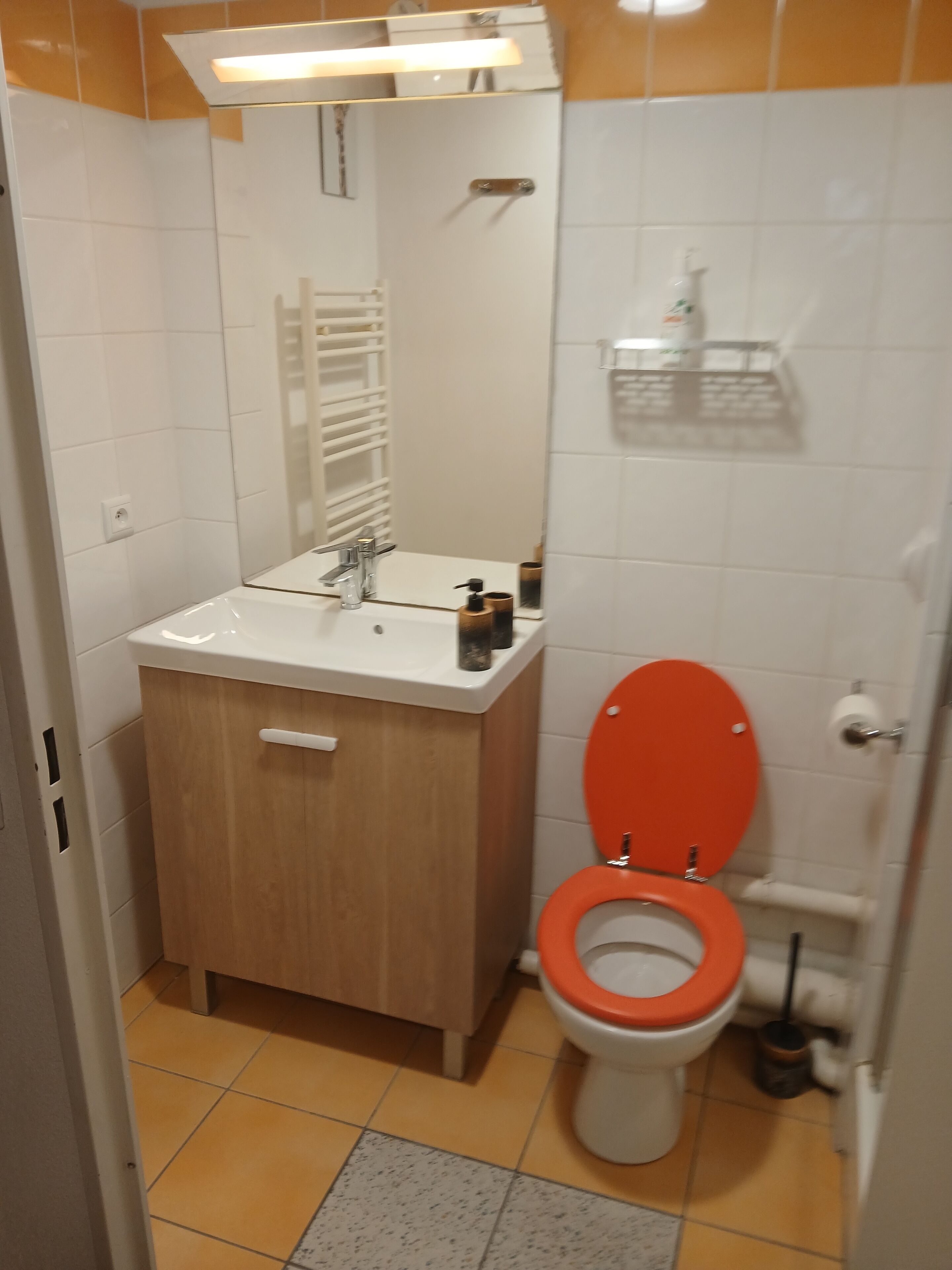 Une salle de bain avec un lavabo blanc, un meuble en bois et des toilettes orange.