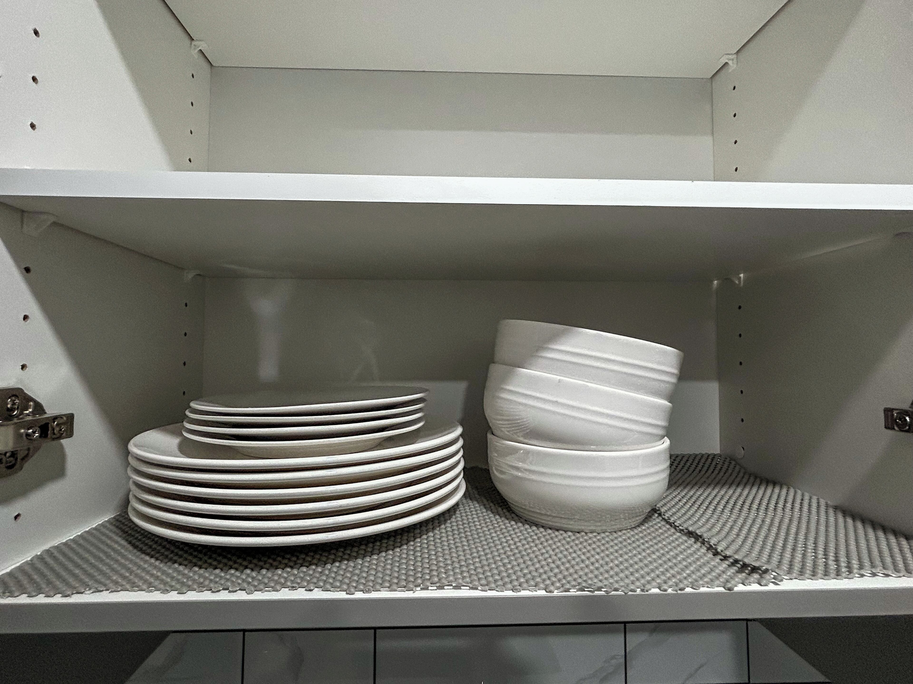 Une étagère de cuisine avec des assiettes blanches empilées et un seul bol blanc.