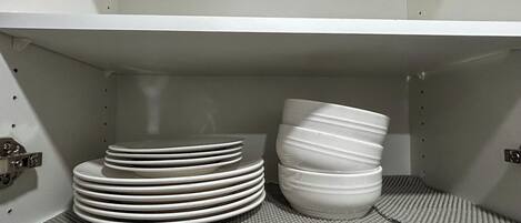 Une étagère de cuisine avec des assiettes blanches empilées et un seul bol blanc.
