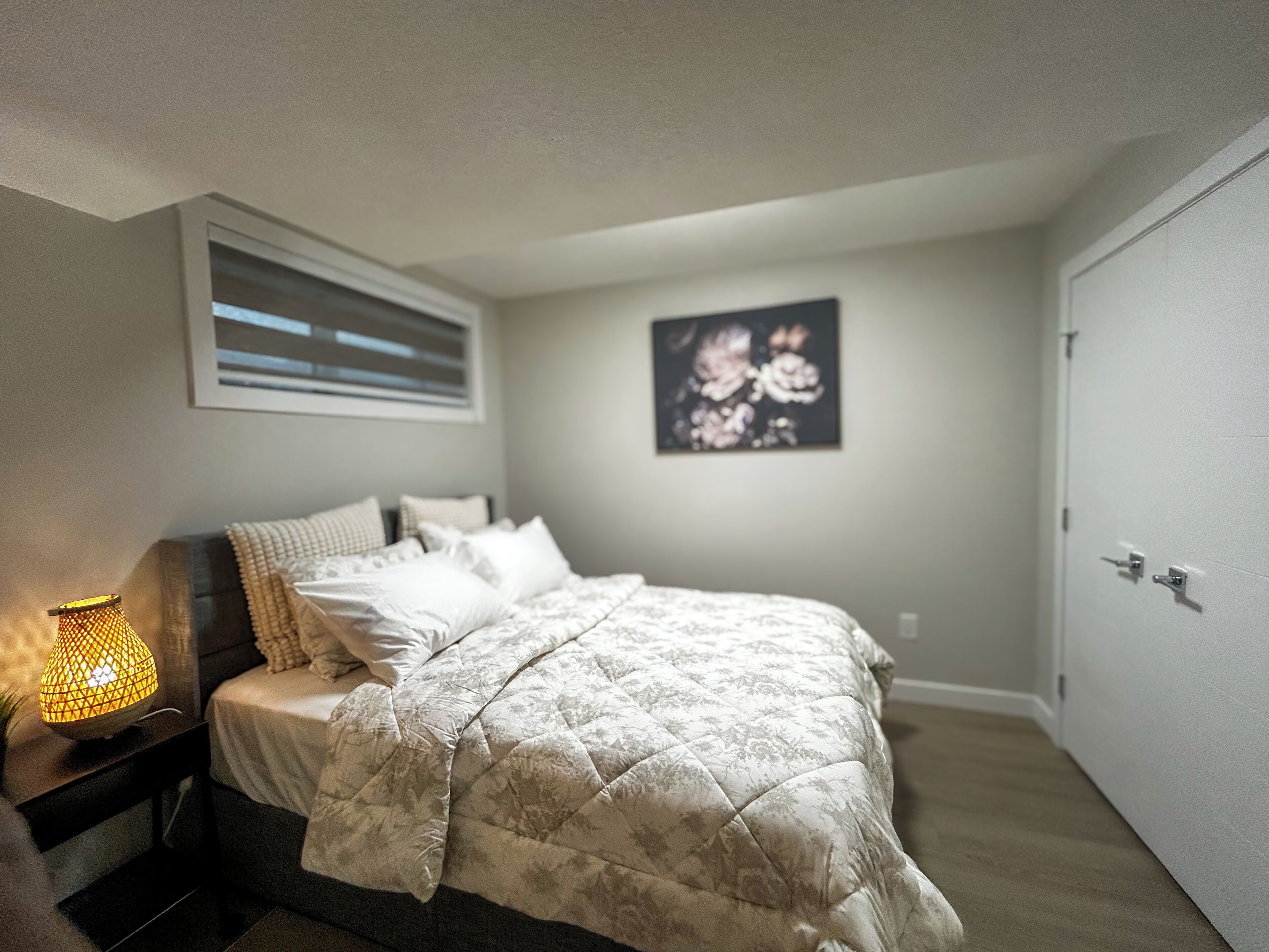 A bedroom with a bed, a nightstand, a lamp, and a wall-mounted picture.