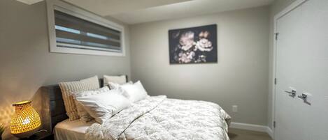 A bedroom with a bed, a nightstand, a lamp, and a wall-mounted picture.