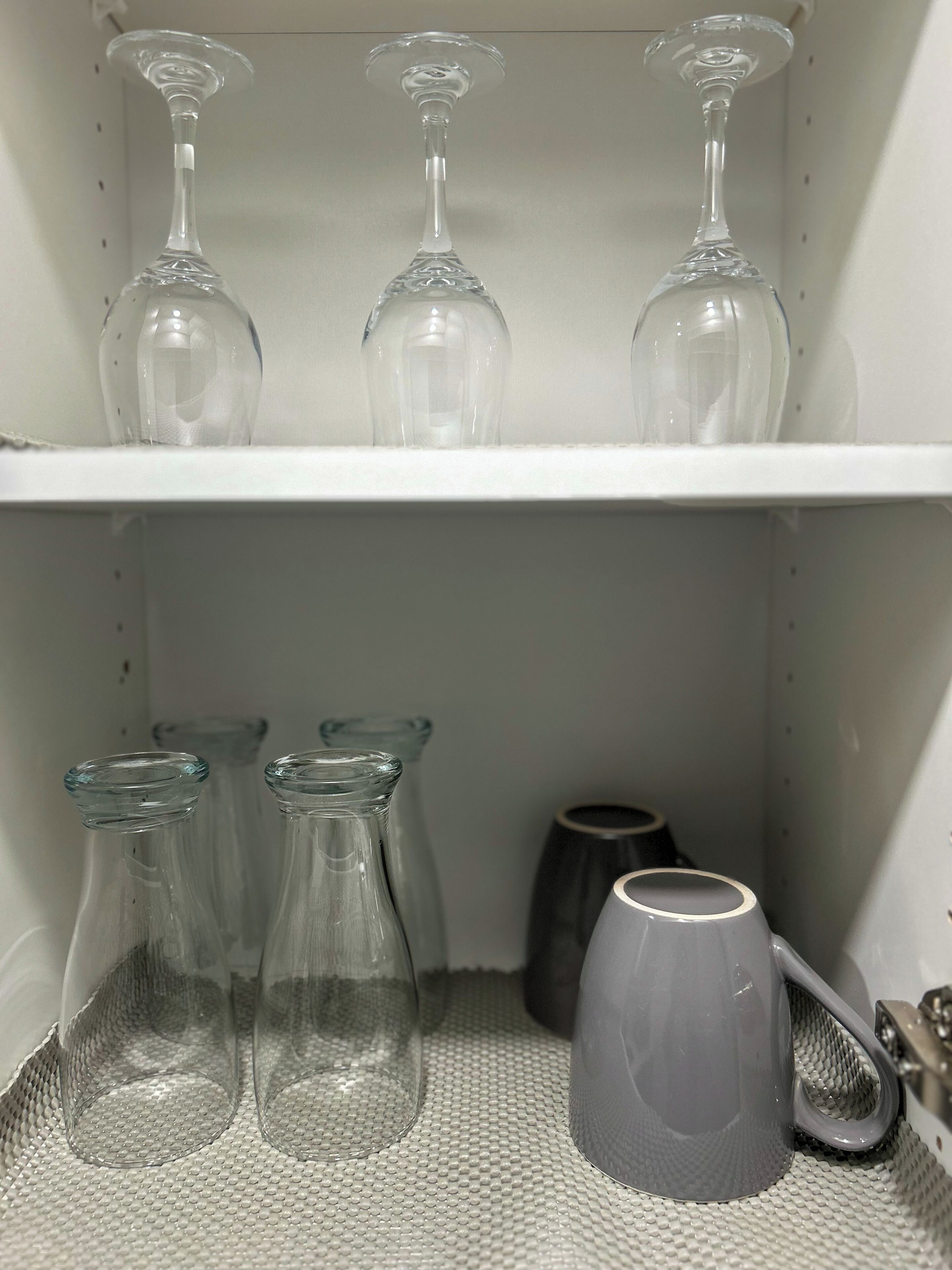 A shelf with three wine glasses and four glass bottles.