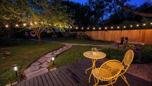 A wooden deck with yellow chairs and a table, surrounded by a stone pathway and a wooden fence. - Stay Vintage at Dandelion (McKinney)