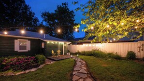 A backyard with a stone pathway leading to a wooden deck, surrounded by a wooden fence and a tree with yellow leaves. - Stay Vintage at Dandelion (McKinney)