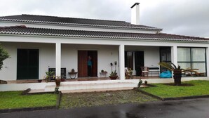 Una casa de dos pisos con tejado de tejas, una chimenea y un porche cubierto con mobiliario exterior.