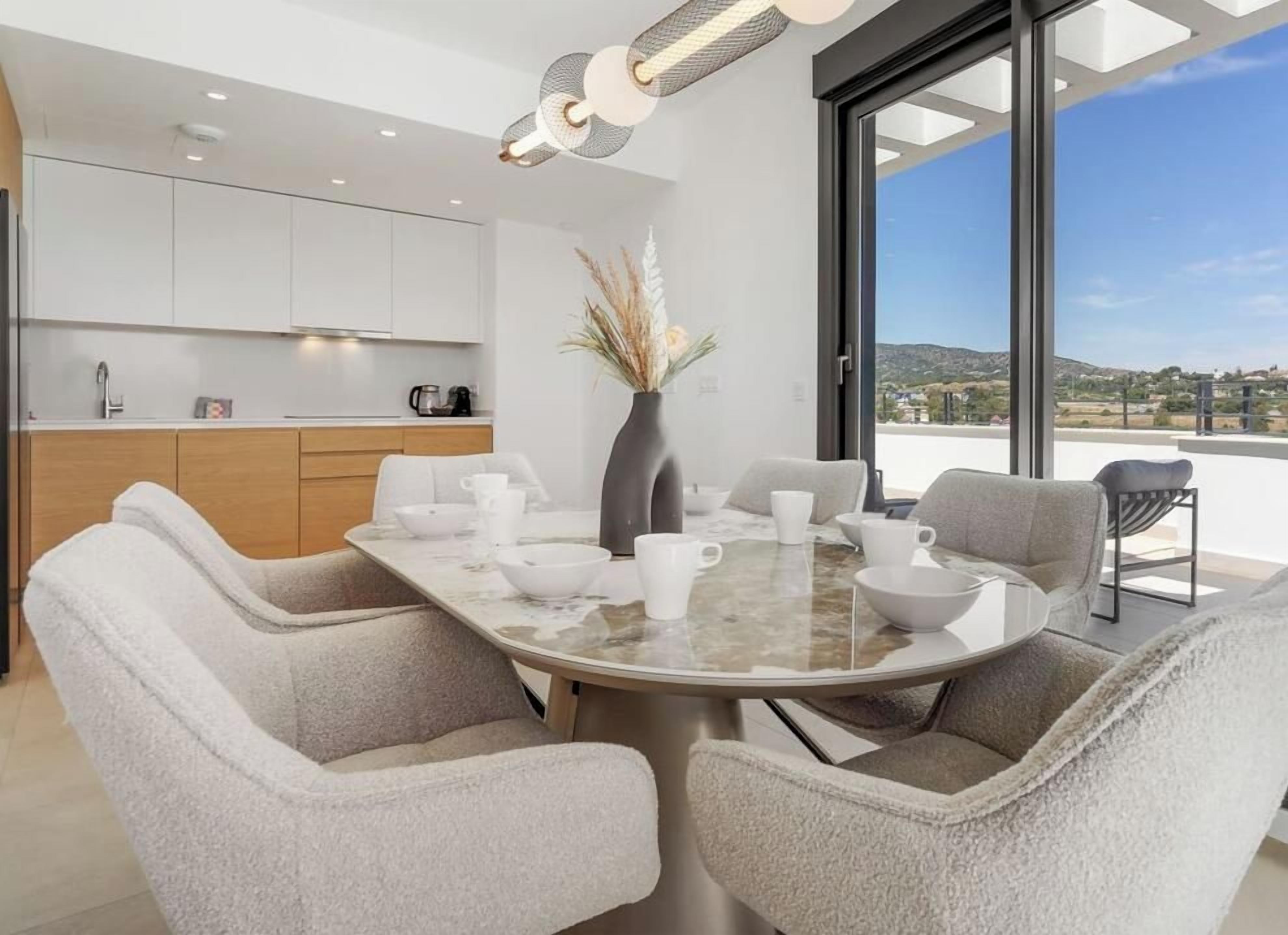 A modern dining area with a round table, six chairs, and a vase with dried plants.