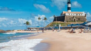 A beach with a prominent lighthouse, sandy shore, and beach chairs.
