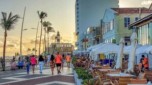 A bustling street with outdoor seating and palm trees, suggesting a lively urban area.