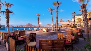 An outdoor seating area with wooden chairs and tables, a fire pit, and a view of the sea and mountains. - Ocean front 2 bedroom Deluxe Suite at Villa Del Palmar Resort Cabo San Lucas (Cabo San Lucas)
