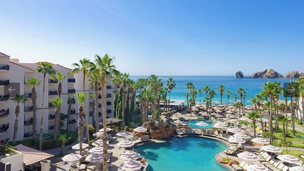 A resort with a central pool surrounded by palm trees and lounge chairs, overlooking a clear blue sea. - Ocean front 2 bedroom Deluxe Suite at Villa Del Palmar Resort Cabo San Lucas (Cabo San Lucas)