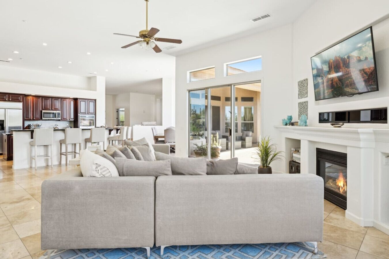 A modern living room with a sectional sofa, a fireplace, a TV, and a kitchen in the background.