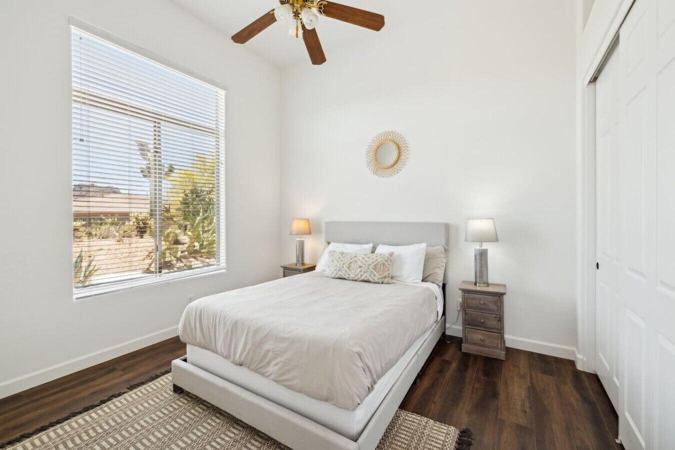 A bedroom with a bed, bedside tables, a ceiling fan, and a view of the outdoors.