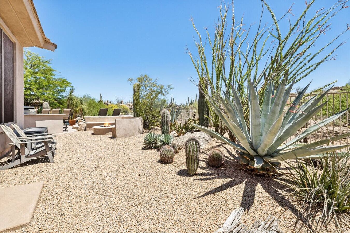An outdoor patio with a fire pit, seating, and various desert plants.