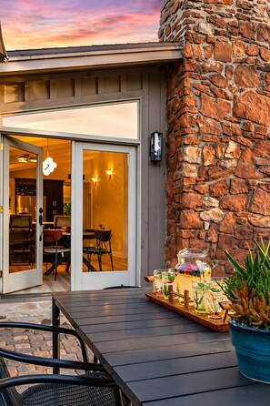 A patio with a stone wall, a glass door leading to an interior dining area, and a tray with beverages and snacks. - Redscape, Near Great Hiking, Views, Hot Tub, Firepit-Charming Design (Sedona)