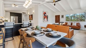 A modern kitchen with a dining area, featuring a large island, wooden chairs, and a view of the living room with a sofa and a coffee table. - Redscape, Near Great Hiking, Views, Hot Tub, Firepit-Charming Design (Sedona)