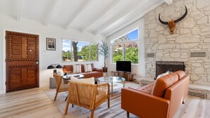 A spacious living room with a stone fireplace, a large wooden door, and a television. - Redscape, Near Great Hiking, Views, Hot Tub, Firepit-Charming Design (Sedona)